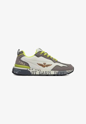 Sneaker low-top grigio e bianco con accenti giallo neon, emblema alato sul lato, scritta sulla suola e "F35 A" sul tallone.