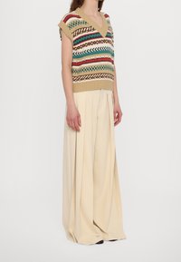 Top de punto sin mangas con cuello en V y patrones geométricos multicolores; combinado con pantalones anchos y plisados en beige; textura suave, ajuste relajado.