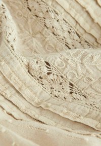 Tissu en lin beige doux avec des détails en dentelle complexes et des rayures texturées. Présente des motifs floraux délicats et des accents en relief.