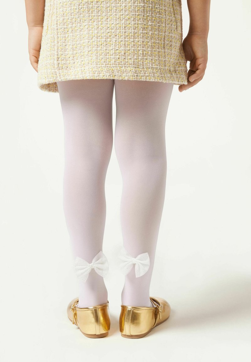 Collant bianchi con un aspetto testurizzato, caratterizzati da due fiocchi in satin bianco alla caviglia; abbinati a scarpe basse metalliche dorate.