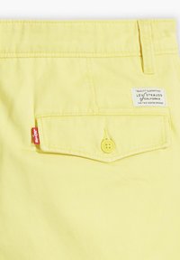 Gula denimshorts med bakficka, med knappstängning och en Levi's-etikett. Slät textur och skräddarsydd design.