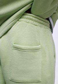 Lichtgroene sweatpants met een elastische tailleband, voorzien van een gestikt zakje aan de zijkant, gemaakt van zachte, gladde stof.