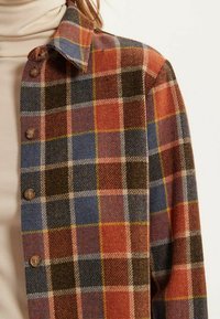 Chemise à carreaux avec des couleurs marron, rouge, bleu et jaune. Fabriquée en tissu texturé, elle dispose d'un devant à boutons et d'un col pointu.
