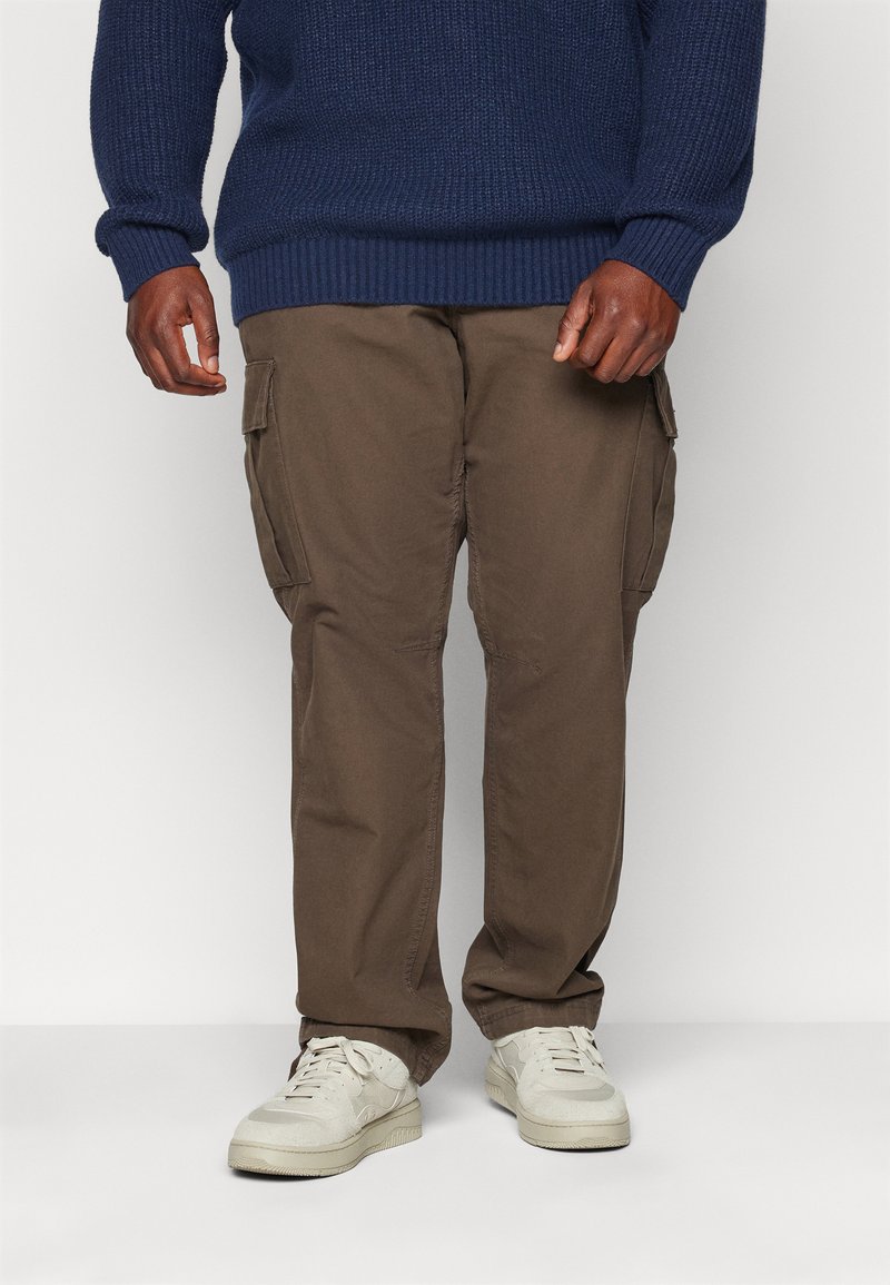 Bruine cargobroek met zijzakken, gemaakt van stevig materiaal; gecombineerd met lichtgekleurde sneakers en een geweven blauwe trui.