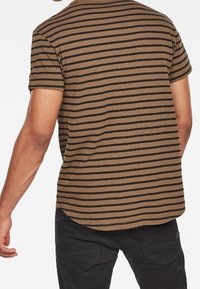 Camiseta a rayas en tela marrón y negra. Manga corta, dobladillo redondeado y un ajuste relajado. Costuras visibles y una textura suave.