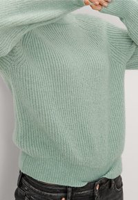 Maglione lavorato a maglia verde menta con finitura testurizzata, orlo e polsini a coste, e un fit rilassato. Jeans scuri visibili in fondo.