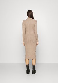 Abito midi in maglia beige con costine verticali, maniche lunghe e scollo rotondo, abbinato a stivali neri chunky.
