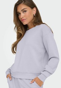 Sudadera de color púrpura claro hecha de una tela suave, con cuello redondo, mangas largas, puños acanalados y bolsillos laterales.