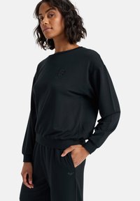 Zwarte sweatshirt met lange mouwen, ronde hals en ribgebreide manchetten. Heeft een subtiele logo in het midden, met een losse pasvorm en een zachte stof.