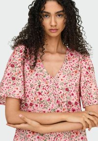 Ziedu raksta kleita gaisā rozā krāsā ar īsām piedurknēm un V formas izgriezumu. Funkcijas mazus sarkanos un zaļos ziedus ar faktūrētu audumu.