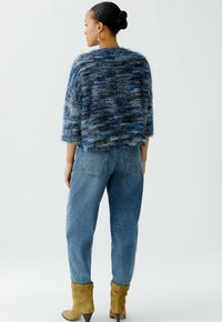 Flauschiger blauer, cropped Pullover mit einem strukturierten Muster, kombiniert mit hellblauen, hochgeschnittenen Jeans und tanfarbenen kniehohen Stiefeln. Rückansicht.