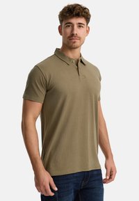 Oliven grøn polo skjorte med klassisk krave, kortærmede og to-knaps lukning. Stoffet er glat og fremhæver en tætsiddende silhuet.