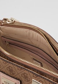Brązowa torebka w wzory z złotym okuciem i zapięciem na zamek. Wewnątrz znajdują się liczne przegrody wykończone gładkim, jasnobrązowym materiałem.