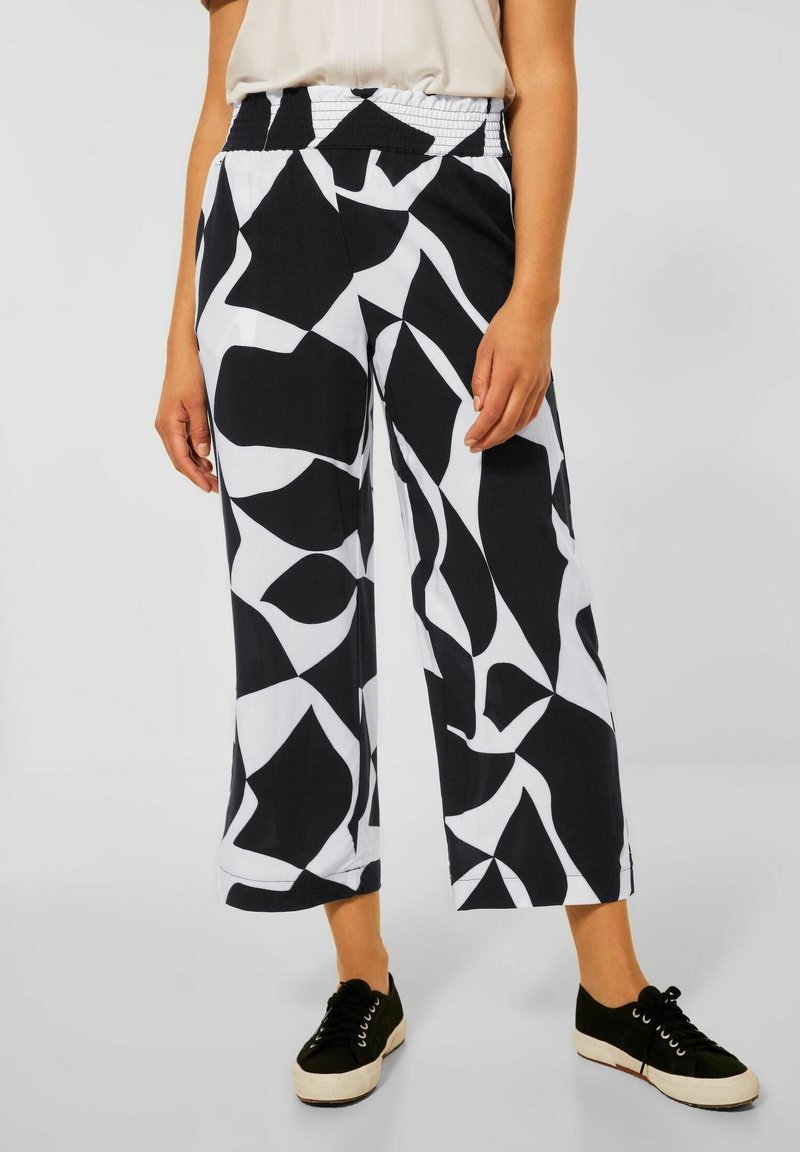 Černobílé vzorované široké kalhoty s gumičkovým pasem a lehkým materiálem, zkombinované s černými teniskami.