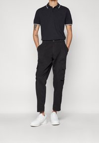 Polo shirt bleu marine avec des accents de col blanc, associé à un pantalon cargo noir avec des poches latérales et des baskets blanches. Style décontracté.
