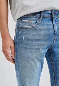 Ljusblå denimjeans med slim fit, lätt slitningar på låren och kontrasterande sömmar på fickorna.
