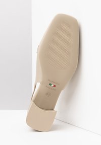 Scarpa beige con tacco, suola testurizzata, punta quadrata e dettaglio a taglio. Include il marchio sulla suola ed è etichettata "Made in Italy".