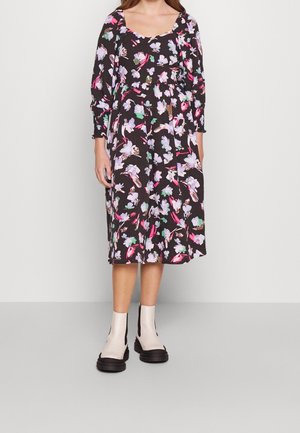 Tummaa ruskeaa kukallista midi-mekkoa, jossa on pitkät hihat ja kuvioina violetin, vaaleanpunaisen ja vihreän sävyiset kukat; yhdistetty kermaisiin nilkkureihin.