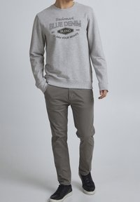 Sudadera gris con texto y logo en negro, combinada con pantalones gris claro y zapatillas negras. La tela parece suave y de diseño casual.