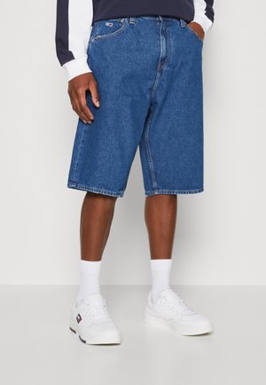 Denim shorts in mediumblauw met een losse pasvorm, voorzien van gestikte naden en een voorzak, gecombineerd met witte sneakers en sokken.
