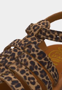 Κοντινή λήψη των λουριών σανδαλιών με καφέ και μαύρο μοτίβο λεοπάρδαλης και αγκράφα κλειδώματος.