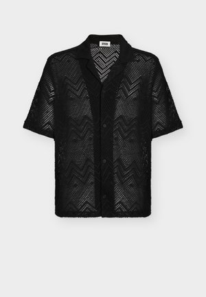 Camisa negra de manga corta con botones, patrón de zigzag de punto abierto y cuello ancho, con etiqueta "DRYKORN" en el interior del escote.