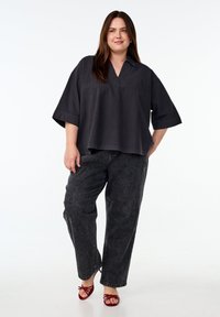 Dunkelgraue, übergroße Bluse mit V-Ausschnitt und weiten Ärmeln, kombiniert mit locker sitzenden, dunkelblauen Denim-Jeans; Modell trägt rote Riemchenhighheels.