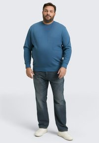 Niebieska bluza z okrągłym dekoltem i ściągaczami, w połączeniu z ciemnymi dżinsami i białymi trampkami. Prosty, luźny krój i gładka tekstura.