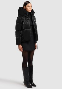 Črna, sijoča puhovka z visokim ovratnikom, z zapiranjem na zadrgo in stranskimi žepi. Kombinirana s črno krilo in visokimi črnimi škornji s peto.