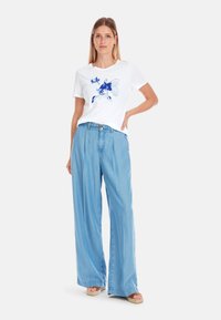 White short-sleeve t-shirt featuring a blue fish graphic paired with light blue wide-leg denim pants. Smooth fabric, relaxed fit, casual style.