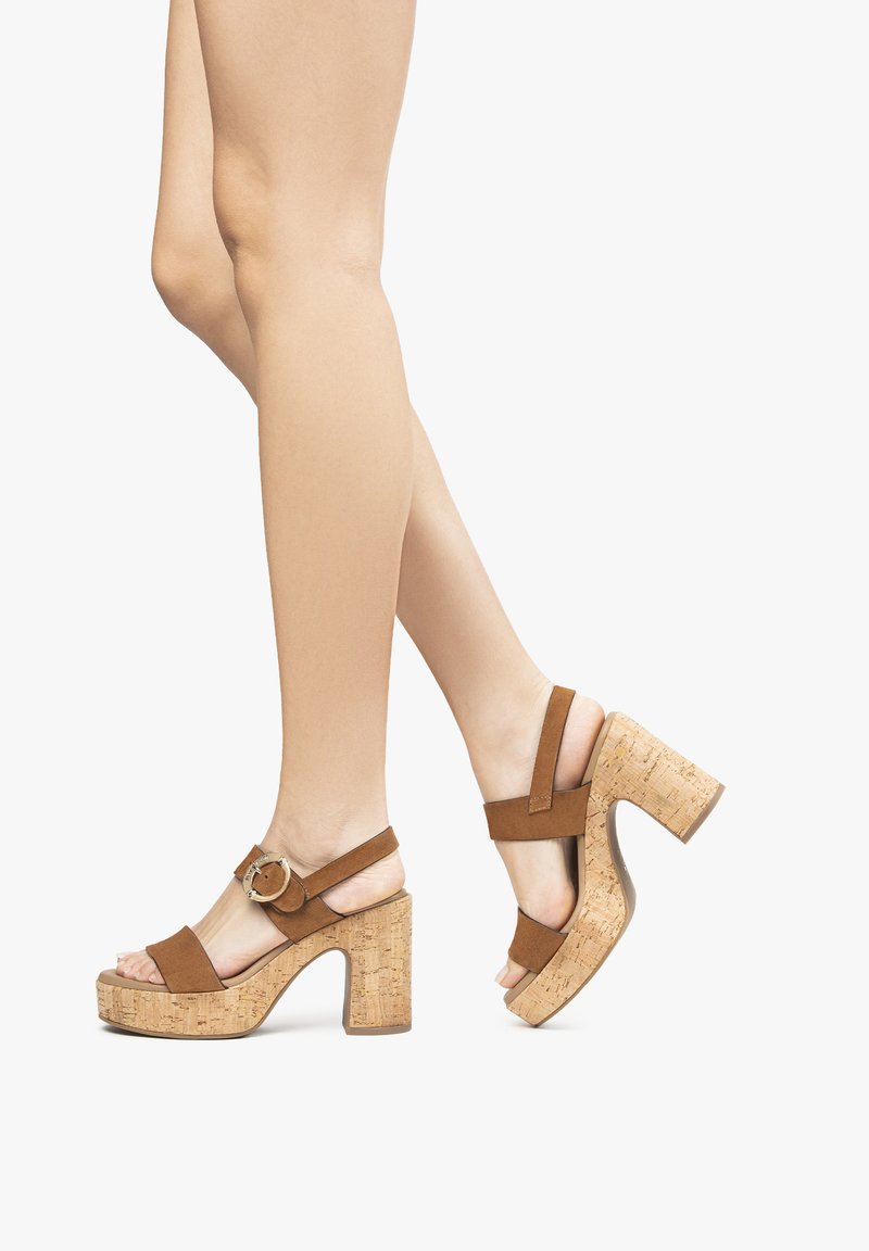 Sandales à talons en suede marron avec plateforme en liège et talon bloc, dotées de brides de cheville et d'un détail de boucle circulaire.