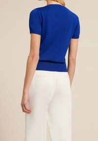 Kortärmad, figurnära topp i livfull blåstickad tyg med ribbade detaljer vid ärmar och nederkant, tillsammans med krämfärgade byxor.