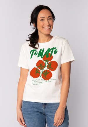 T-shirt en coton blanc avec un graphique de tomates rouges et un texte vert. Le design comprend des lettres en gras et des accents dessinés à la main.