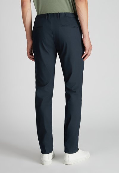 Granatowe spodnie o gładkiej fakturze, zwężanym kroju nogawek i elastycznym pasie. Posiadają dwie tylne kieszenie i są zestawione z białymi trampkami.