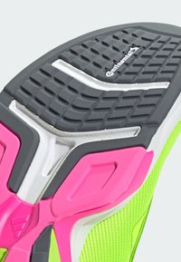 Schoenzool met een gestructureerde grijze rubberen oppervlakte, roze en witte accenten, en een levendige neon groene netupper voor extra contrast.