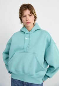 Hoodie bleu clair en tissu doux avec une poche avant, une capuche à cordon et un petit logo Nike blanc sur la poitrine.
