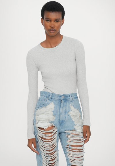 Camisola cinza de manga longa com nervuras, combinada com jeans de ganga azul clara desgastados apresentando grandes rasgos e bordas desfiadas.