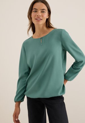 Blouse à manches longues teal en tissu lisse, mettant en avant un col rond avec un petit détail en œillet et des poignets froncés.