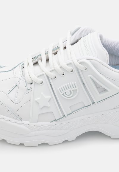 Baltas atlikts sneakers ar tekstūrētu gumijas zoli, auklu dizainu, dekoratīviem akcentiem, tostarp zvaigzni un aci, un izšūtu detaļu.