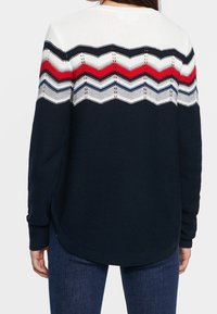 Strickpullover mit einem weißen und marineblauen Zickzackmuster und roten sowie blauen Akzenten, aus strukturiertem Stoff, mit langen Ärmeln und abgerundetem Saum.