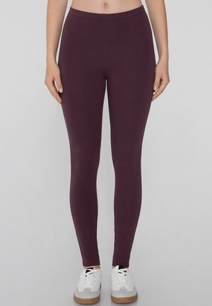 Leggings burdeos hechos de una tela elástica con una textura suave, con una cinturilla alta y un ajuste ceñido, combinados con zapatillas deportivas blancas.