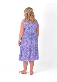 Purple floral-patterned maxi dress with a tiered skirt and a smocked bodice. Sleeveless design, lightweight fabric, paired with slide sandals.