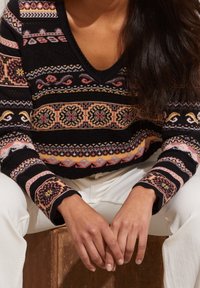 Sweter dzianinowy z dekoltem w kształcie V, w czarnym kolorze, z kolorowymi wzorami kwiatowymi i geometrycznymi oraz długimi rękawami z wzorzystymi mankietami.