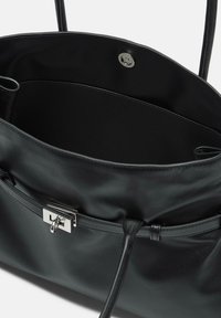 Czarna skórzana torebka o gładkiej fakturze, z zapięciem na magnes i regulowanym sznurkiem. Wnętrze jest niepodszewkowane i przestronne.