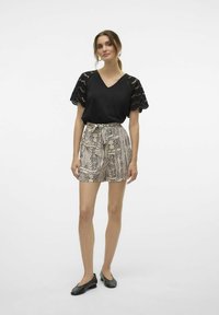 Haut noir à manches courtes avec des détails en dentelle, associé à un short beige à motifs avec une taille à nouer. Des chaussures plates noires complètent le look.