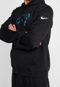 Schwarzer Kapuzenpullover mit einem blauen Panther-Graphic auf der Vorderseite und einem weißen Nike-Logo an den Ärmeln. Weicher, strukturierter Stoff.