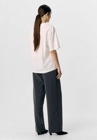 Camiseta de algodón de color claro con mangas cortas, combinada con pantalones de pierna ancha de talle alto en gris oscuro y tacones negros de puntera.