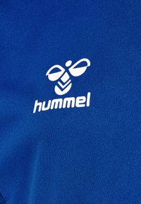 Niebieska tkanina z białym logo "hummel" oraz abstrakcyjnym wzorem pszczoły, charakteryzująca się gładką teksturą i żywym kolorem.