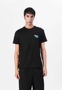 Black cotton t-shirt featuring a small turquoise "Tommy Jeans" logo on the chest. Classic crew neck design with short sleeves.