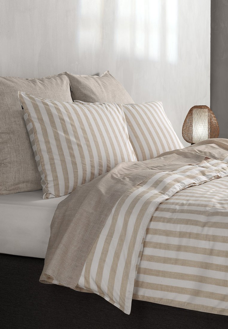 Gestreifte Bettdecke aus beige und weißem Stoff; passende gestreifte Kissen; strukturiertes beige Akzentkissen; minimalistische gewebte Lampe.